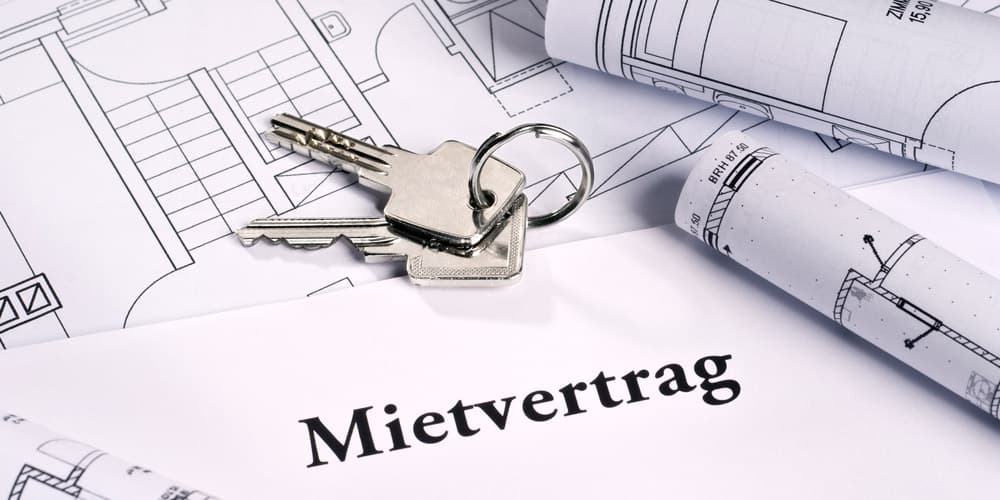 Clés posées sur un contrat de location allemand et des plans techniques de construction.